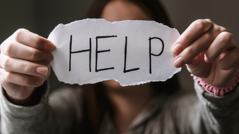 woman holding up a sign with the word "help" written out