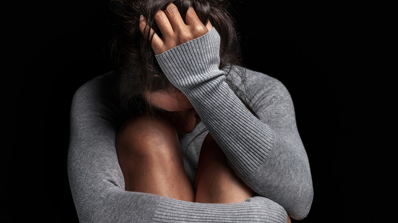 upset woman in a gray sweater hugging her legs and holding her head in her hand