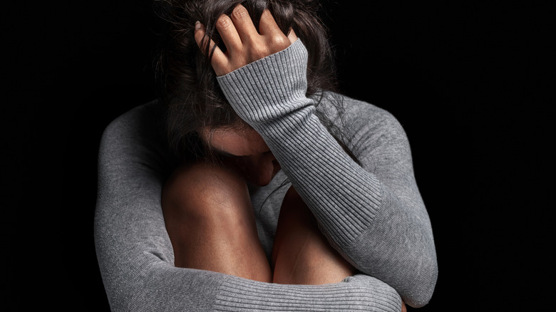 upset woman in a gray sweater hugging her legs and holding her head in her hand