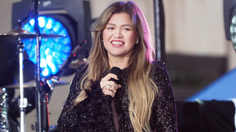 Kelly Clarkson smiling while performing onstage in a sparkly black dress
