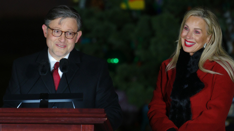 Mike Johnson speaks at podium while Kelly Johnson forces awkward smile