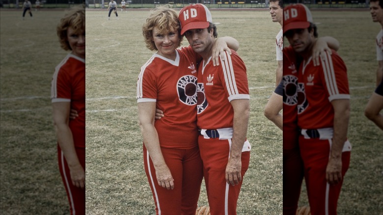 Marion Ross and Henry Winkler wearing softball uniforms with their arms around each other