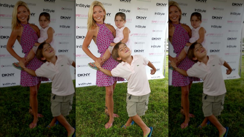 Kelly Ripa holds her daughter, Lola, and smiles next to son Michael