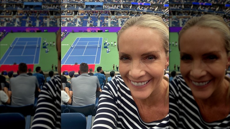 Dana Perino smiling in a black and white striped suit while attending a sports game.