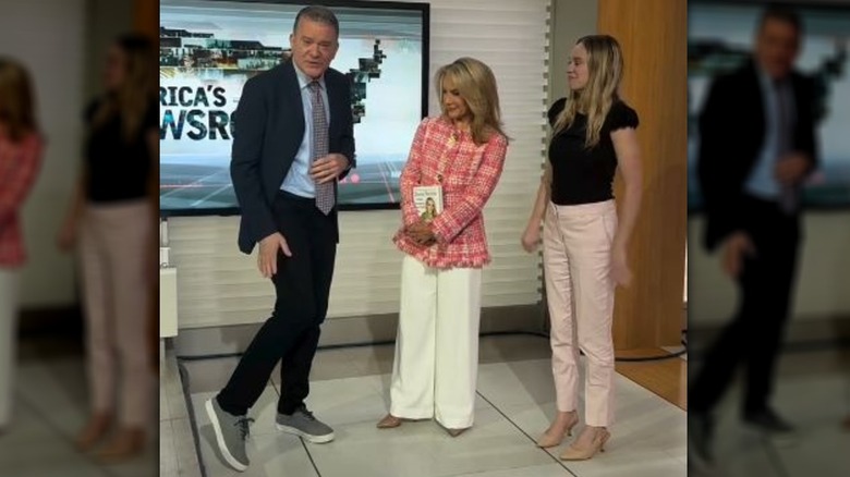 Dana Perino looks over at Paul Mauro who poses with his leg bent.