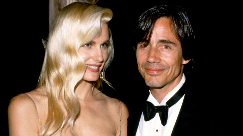 Daryl Hannah and Jackson Browne stand next to each other at a black tie event while Hannah looks off camera smiling with her hair down and slightly curled