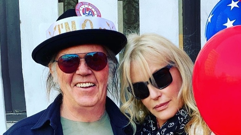 Daryl Hannah smiles next to Neil Young both wearing sunglasses outside next to balloons