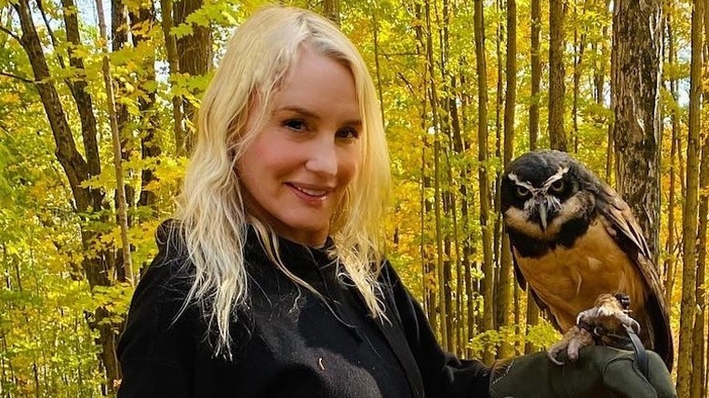 Daryl Hannah smiles outside holding an owl on her arm in the woods