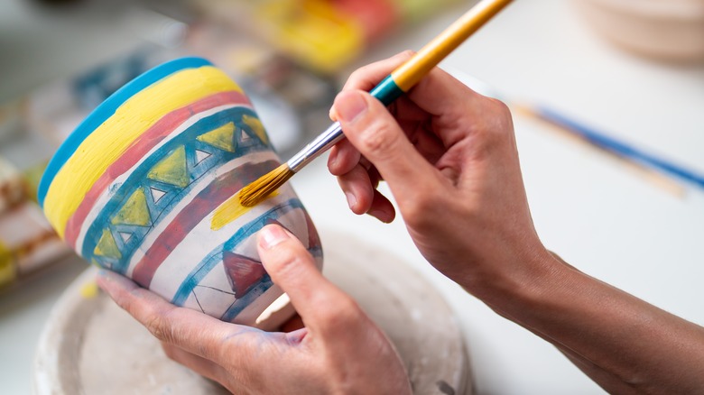 Hands painting a ceramic pot 
