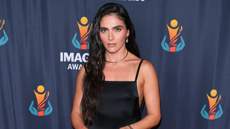 Arienne Mandi posing in a black dress with spaghetti straps.