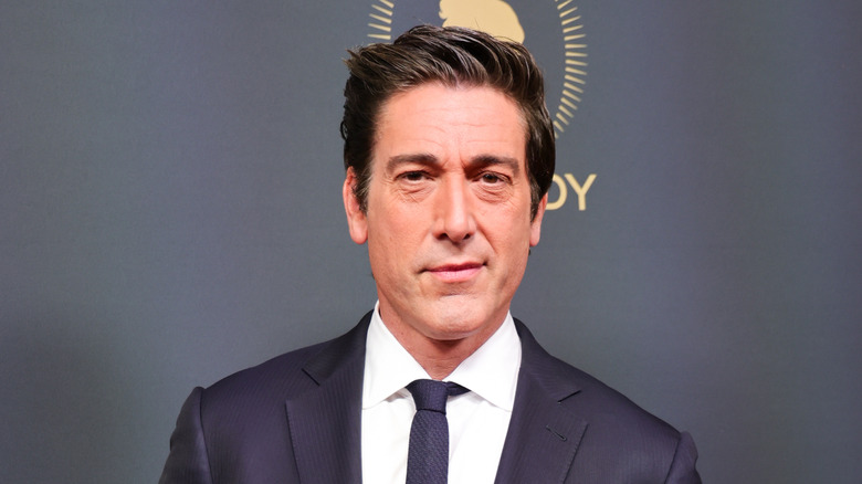 David Muir posing in a dark suit at an event