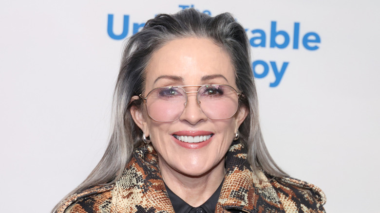 Patricia Heaton smiling in an orange and tan coat while wearing glasses.