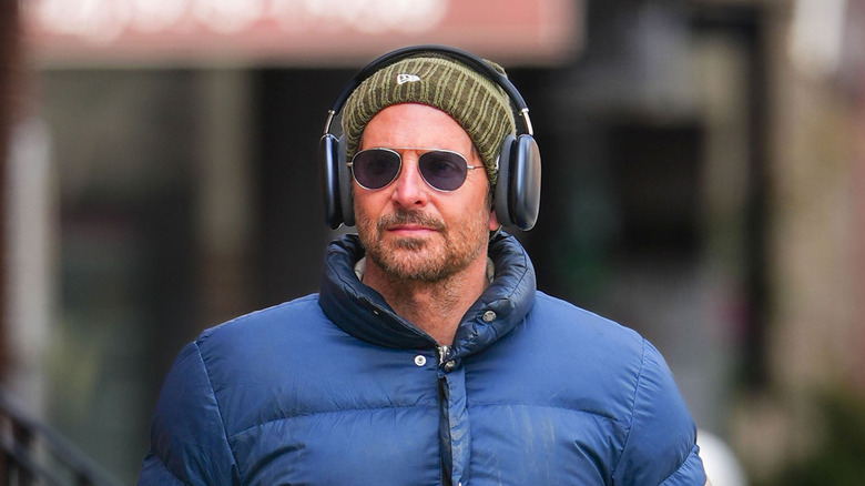 Bradley Cooper in a blue puffer jacket and green beanie with headphones on top