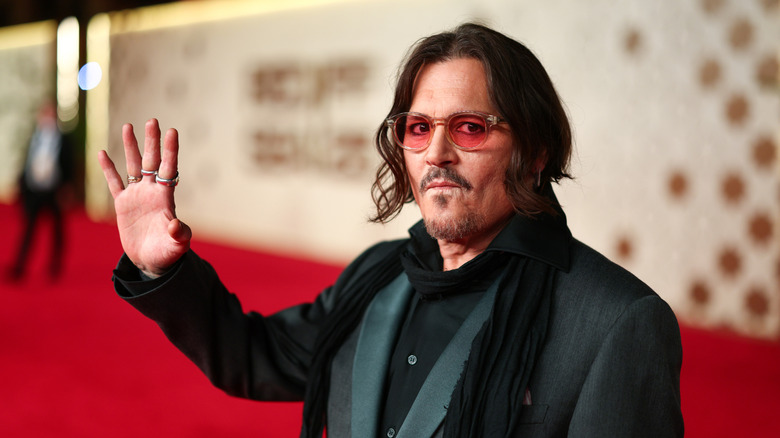 Johnny Depp waving on the red carpet wearing red glasses and green blazer