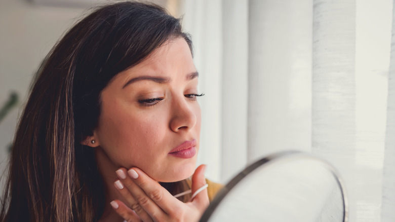 A woman inspecting her skin in a mirror 