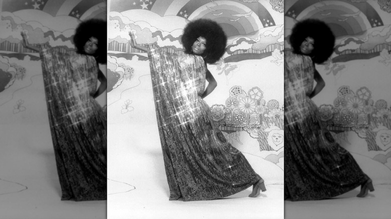 Diana Ross posing in a long draping shimmering gown with one hand out to the side and an afro in front of an illustrated background