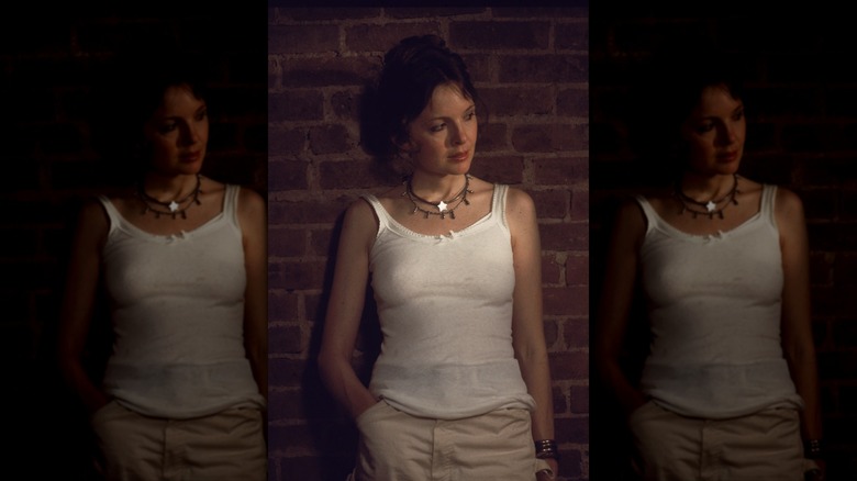 Diane Keaton in a white tank top, leaning back against a brick wall.