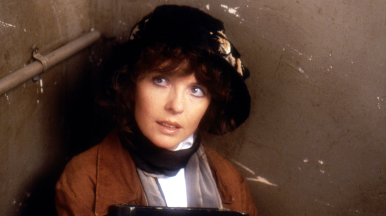 Diane Keaton looking up from a brown corner in a hat.