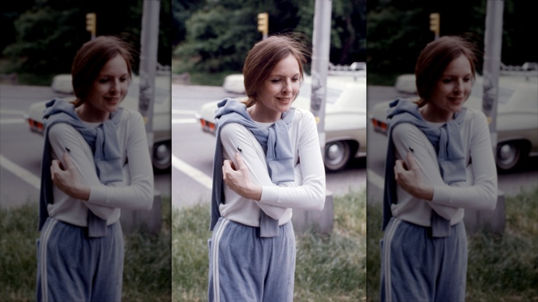 Diane Keaton walking on a sidewalk with her arms wrapped around herself.