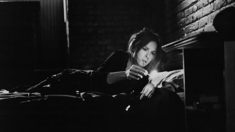 Diane Keaton laying on a bed in black and white, smoking a cigarette.