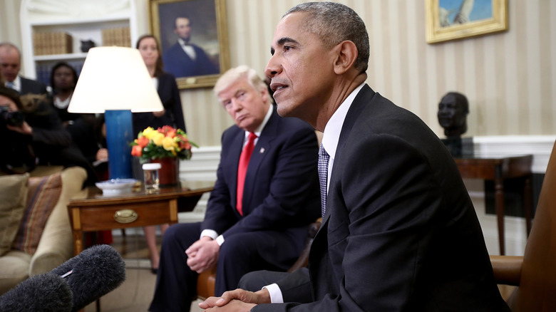 Barack Obama and Donald Trump seated in the Oval Office in suits