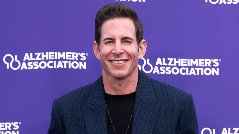 Tarek El Moussa smiling in a blue blazer and black shirt while wearing a silver necklace.
