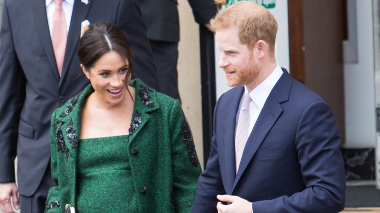 A pregnant Meghan Markle wearing dark green and walking with Prince Harry (2019)