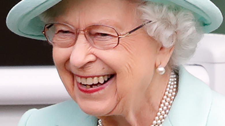 Queen Elizabeth II smiling and looking to the side in turquoise hat