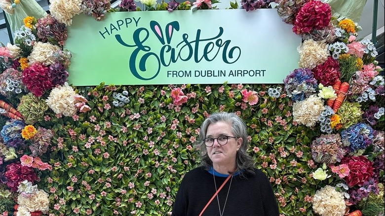 Rosie O'Donnell posing in front of a flower wall and a sign that says Happy Easter from Dublin Airport.