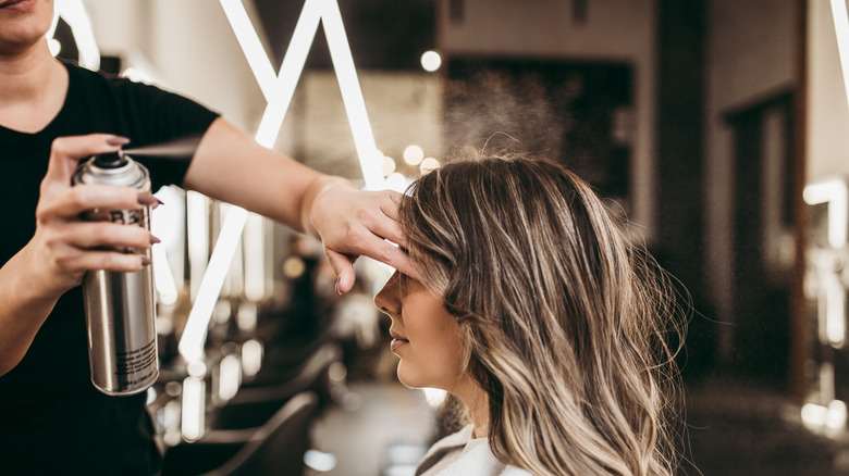 hairstylist shielding a woman's face from hairspray 