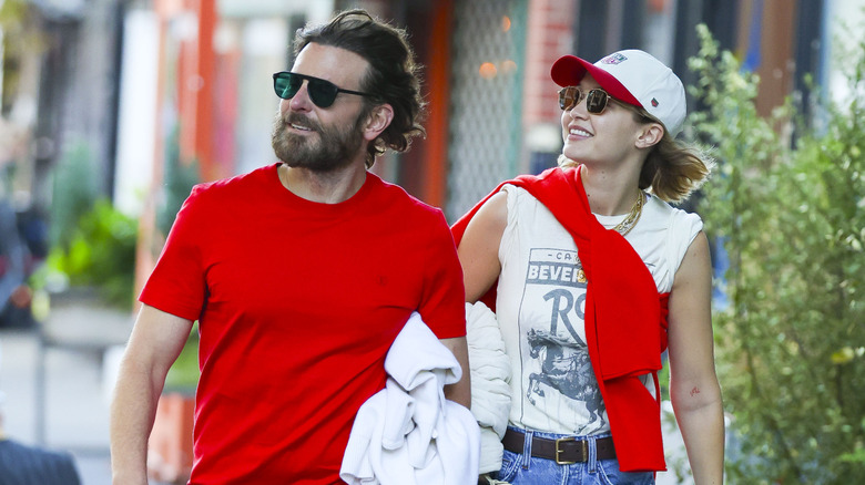 Gigi Hadid and Bradley Cooper smiling while walking together and wearing sunglasses