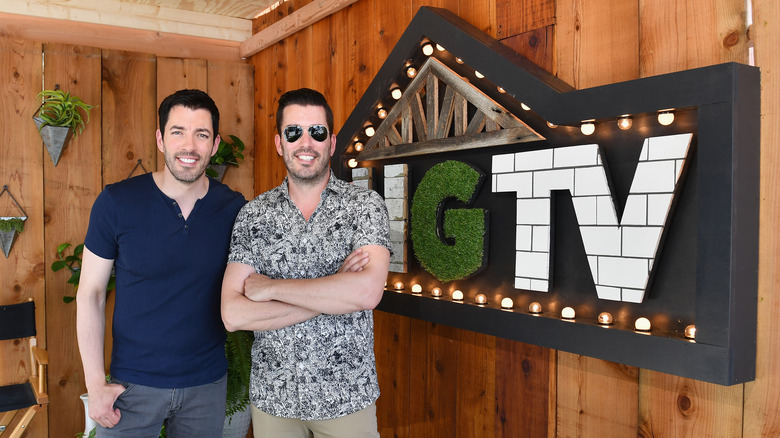 Drew and Jonathan Scott standing in front of an HGTV sign