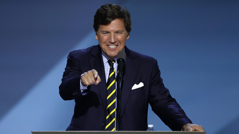 Tucker Carlson smiling at a podium while pointing at his audience