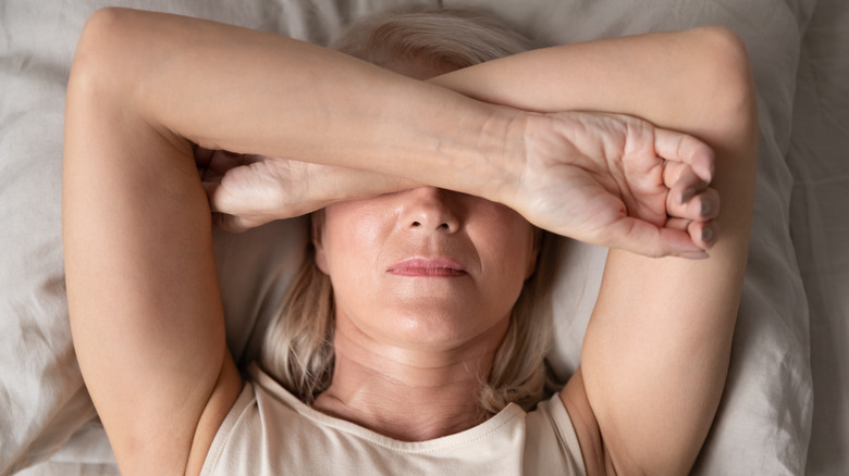 A woman crossing her arms over her face to sleep