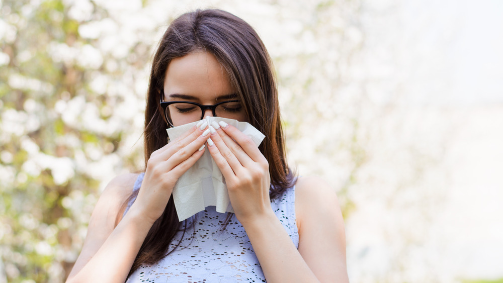 Woman blowing nose in front of flowering trees