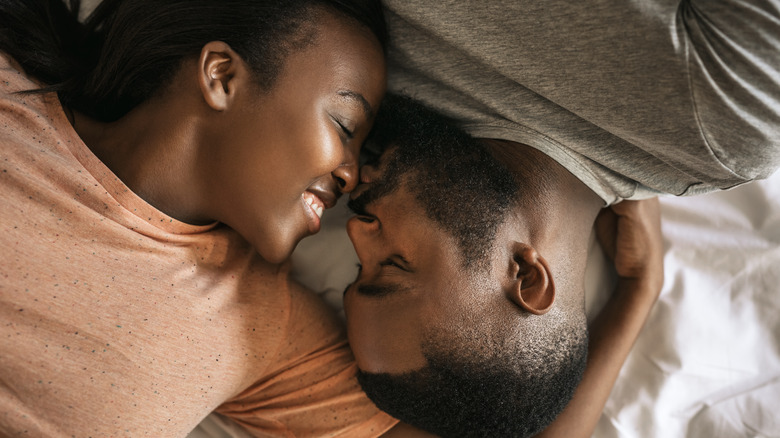 man kissing woman's nose in bed