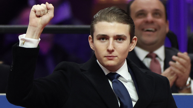 Barron Trump fist-pumping the air in a black suit with slicked-back hair