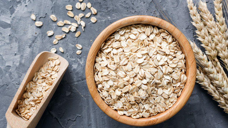 oat flakes in wooden bowl and golden wheat ears on stone background