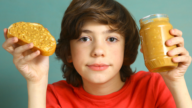 child holding up bread with peanut butter and peanut butter jar