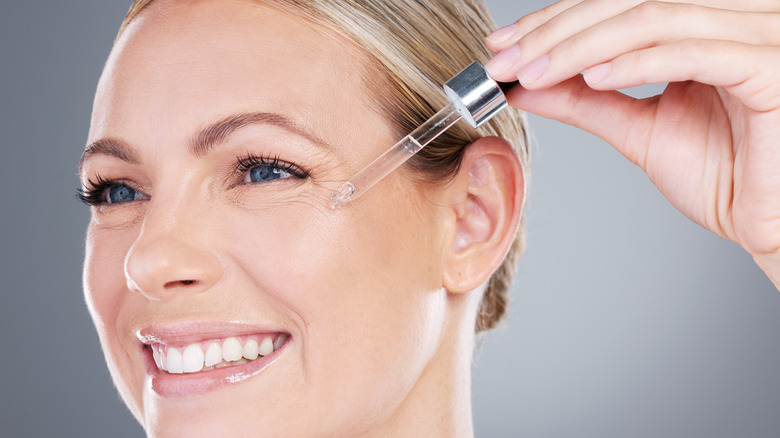 A smiling woman applying serum to her face 