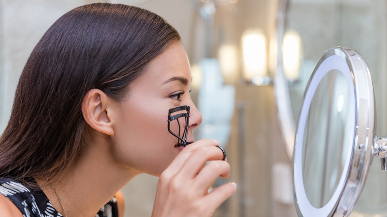 Woman using eyelash curler in magnifying mirror 