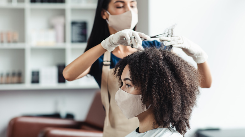 masked stylist trimming client's hair