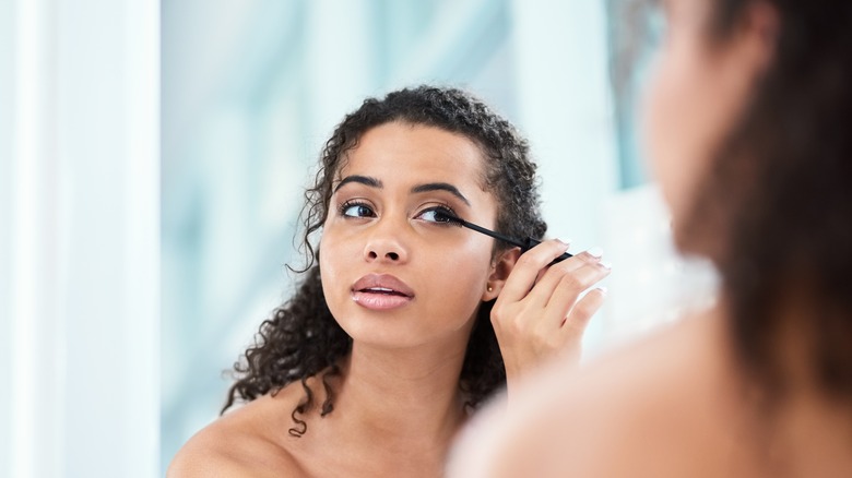 Woman applies mascara in mirror