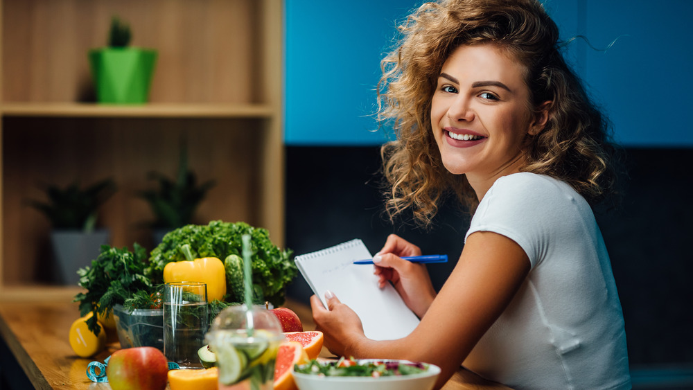 Woman smiling sitting beside vegetables and writing a list