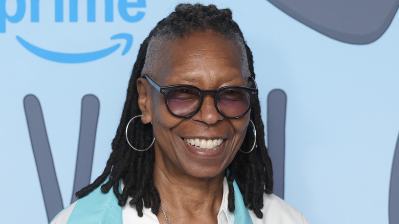 Whoopi Goldberg grinning widely at photographers on the red carpet