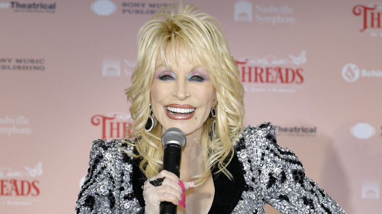 Dolly Parton holds a microphone and smiles