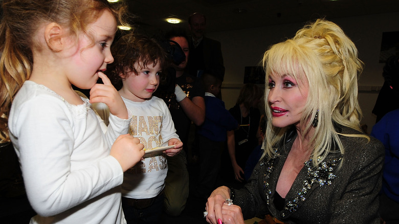Dolly Parton kneeling down to speak to children