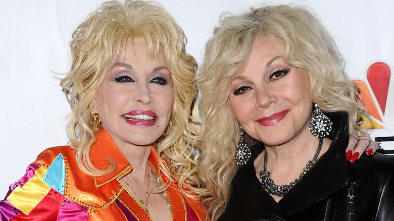 Dolly Parton in a colorful outfit with her arm around Stella Parton in black outfit