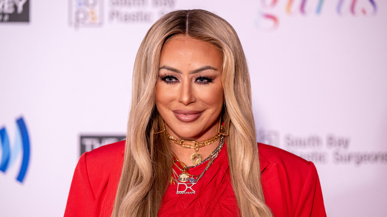 Closeup of Aubrey O'Day on the red carpet with an eclectiv necklace stack and bright red blazer