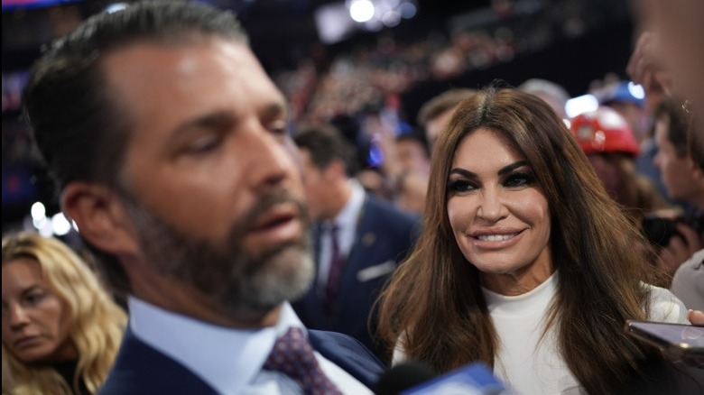 Kimberly Guilfoyle smiling and looking on as Donald Trump Jr. speaks to someone off-camera
